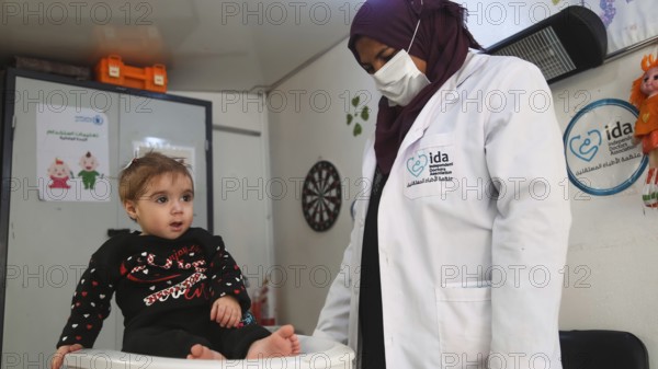 A doctor examining a refugee child for malnutrition in the camp using weight and height measurement
