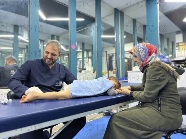 A displaced Syrian child receiving physical therapy from a physiotherapist after a war injury.
