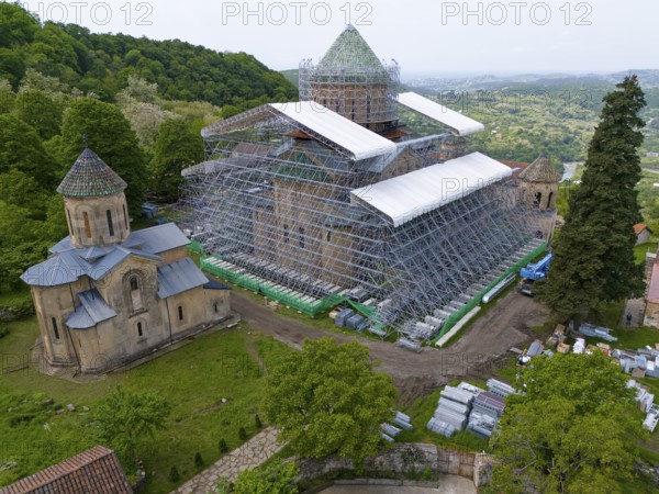 Large church with scaffolding on a hill in a green landscape, aerial view, Gelati Monastery near