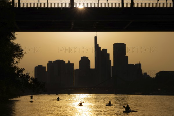 The evening sun stands over the Frankfurt banking skyline while paddlers and rowers navigate the