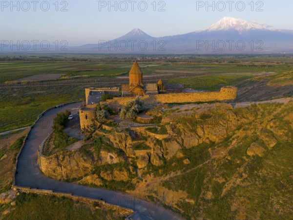 Historic monastery on a rocky hill with a wide view of mountains and plains in the warm light of