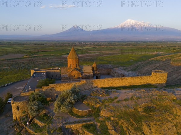 An old church surrounded by walls in front of a mountain range at dawn, aerial view, Chor Wirap