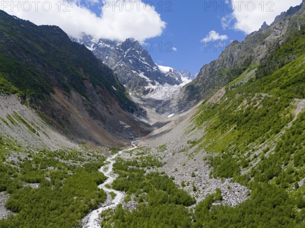 Imposing mountain scenery with glacier in the valley, surrounded by green forests and a meandering