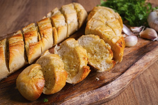 Garlic bread, baguette with garlic butter and herbs, on a wooden board, with herbs and garlic