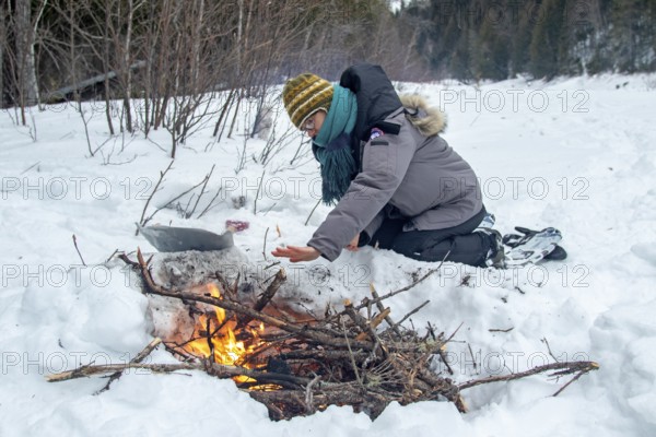 A woman warms herself by a campfire in winter, Gaspesie national park, Province of Quebec, Canada,