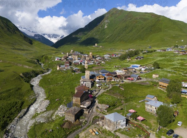 Village with river course, surrounded by green mountains and meadows under a blue sky and striking