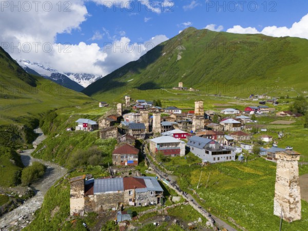 A picturesque mountain village with historic towers and green hills under a blue sky, aerial view,