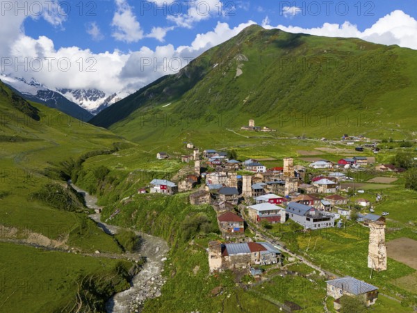 A traditional village with historic towers, embedded in a green mountain landscape, aerial view,