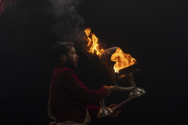 Hindu priest performing the Aarti ritual, holding a burning oil lamp, at the Ganges, Bangali Tola,