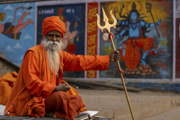 Indian sadhu holding trident, with image of Shiva in the background, Bangali Tola, Varanasi, Uttar