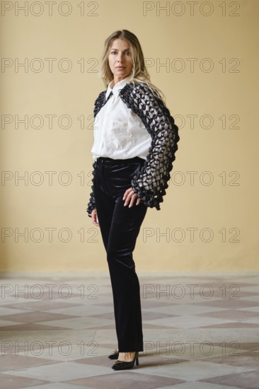 Brightly lit indoor location displays a middle-aged fashion model standing confidently. She wears a