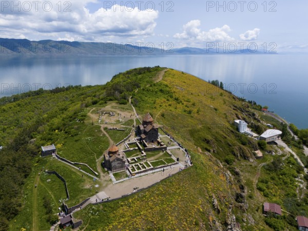 Panorama of a monastery on a green hill with a view of a lake and mountains under a cloudy sky,