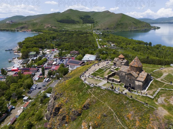Aerial view of a busy monastery on a hill surrounded by a lake, mountains and a small village,