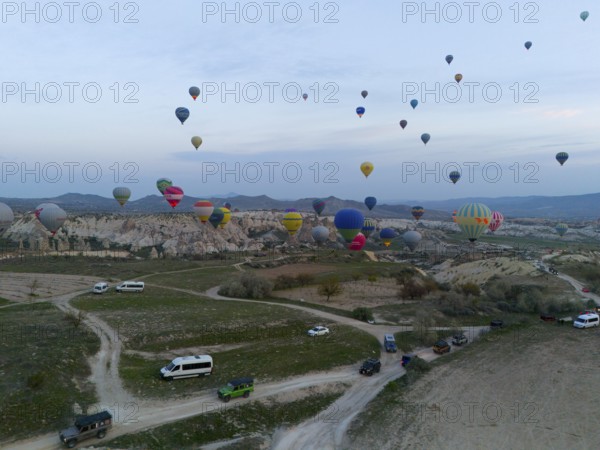 Balloons rise into the sky while vehicles stand on the ground in an open landscape, aerial view,
