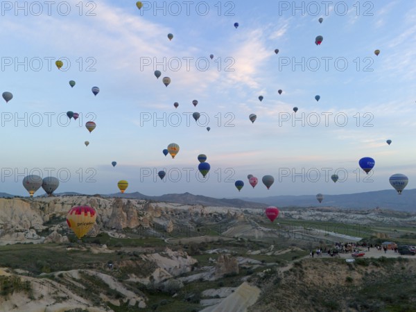 Many colourful hot air balloons float over a vast Turkish landscape in the early morning, aerial