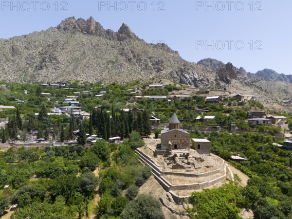Small historic church on a hill with mountains in the background and lush vegetation, aerial view,