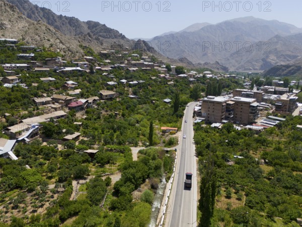 Village with a road winding through a mountainous landscape with green vegetation, aerial view,