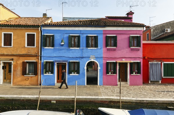 Lone walker on the canal, typical street scene in winter, colourful facades in Burano, island in