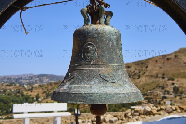 Antique metal bell in rural setting with background landscape and blue sky, Panagia tou