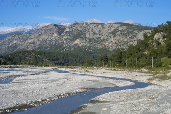 A calm river flows through a wide gravel bed, framed by forested mountains, Dargaz River near