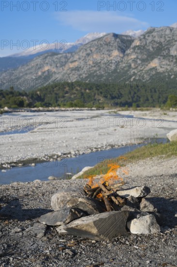 A campfire in a rocky landscape with mountains and a riverbed in the background, Dargaz River near