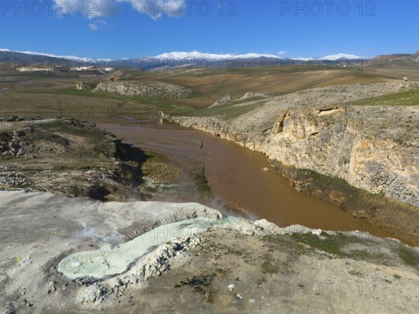 Vast landscape with brown river and rocky gorge under blue sky and white clouds, aerial view,
