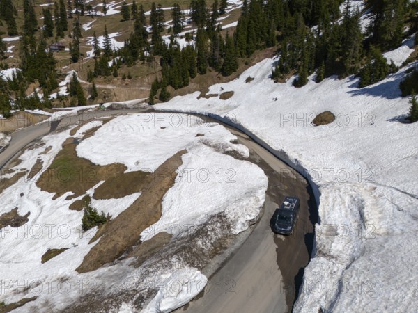 Bird's eye view of a car on a snowy mountain road with curves and fir trees, aerial view, camper,