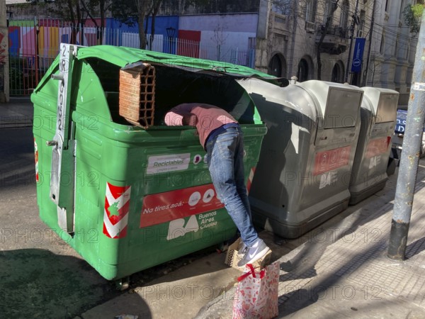 Poverty in Buenos Aires, a homeless man searches for something usable in a rubbish container,