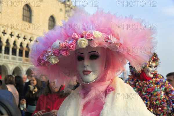 Venetian mask, disguised woman with big pink hat, walker, crowd on St Mark's Square, Carnival in
