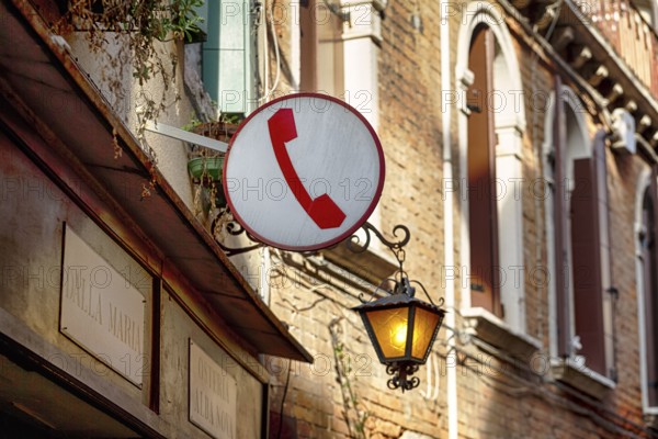 Sign with pictogram, red telephone receiver, public telephone, facade of a restaurant with street