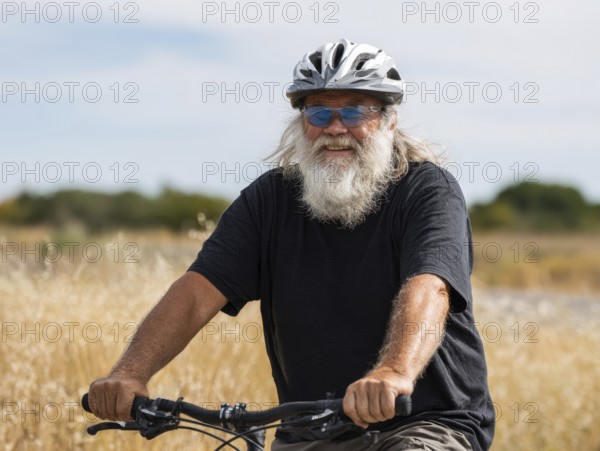 A man, senior citizen with a bicycle helmet rides on a bicycle and smiles friendly into the camera,