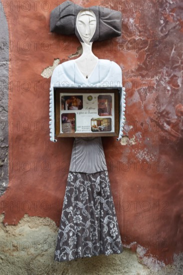 Abstract sculpture of a woman on a rust-red plastered wall. Figure holding a box with photos,