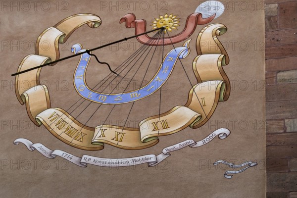 Artfully painted sundial on a sandstone wall with Roman numerals and decorative elements, Alsace,