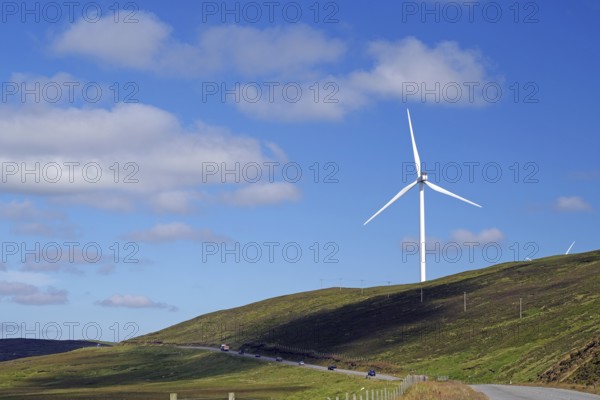 Single wind turbine on a hill next to a road under a blue sky, Mainland, Shetland Islands,