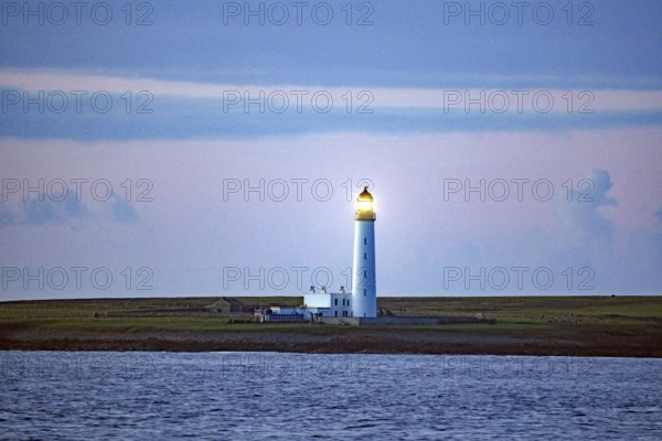 Lighthouse on the coast at dusk with blue sky in the background, crossing between Orkney and