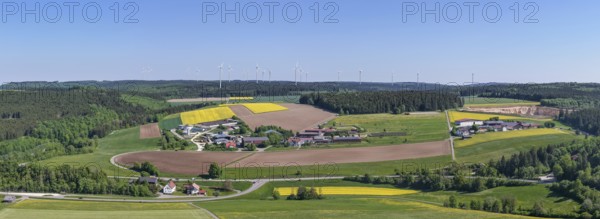 Far-reaching panoramic view of a village with surrounding fields and wind turbines, near