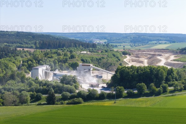 A large industrial plant embedded in a hilly, green landscape, gravel works near Böhmenkirch,