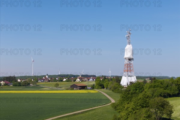 A transmission tower and wind turbines near a village under a blue sky, radio tower being