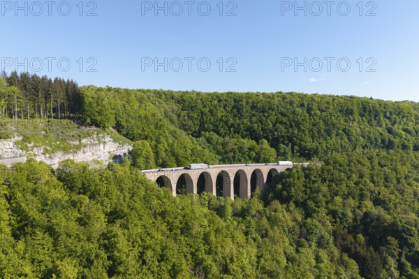 A viaduct leads over a dense forest landscape under a blue sky, Drachenloch bridge on the