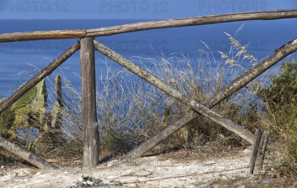 Rustic wooden fence overlooking the blue sea and coastal vegetation, Ricadi, Capo Vaticano