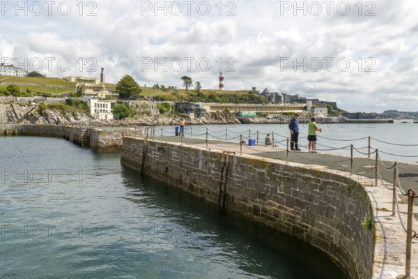 Fishing from harbour wall, seafront coastline waterfront, Plymouth, Devon, England, UK view east to