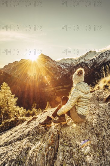 Woman sitting thoughtfully at a feslen at autumn atmosphere during sunset in the Swiss Alps in the