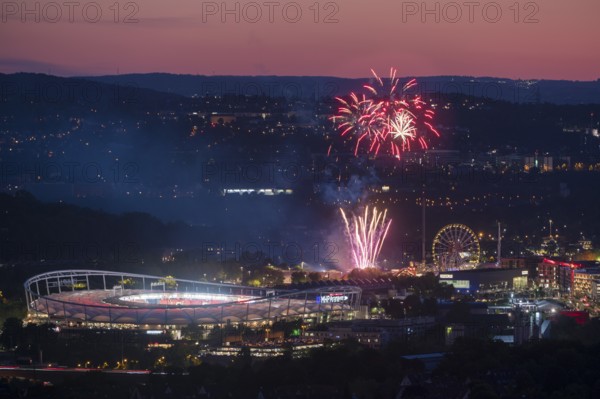 Fireworks at night illuminate the city above a stadium, next to an illuminated Ferris wheel in a