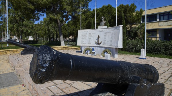 A monument with cannons and bust, surrounded by inscriptions and green vegetation in the open,