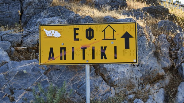 Apitiki, Bunker, Yellow sign with Greek inscription and arrow in front of a rock face, Photos