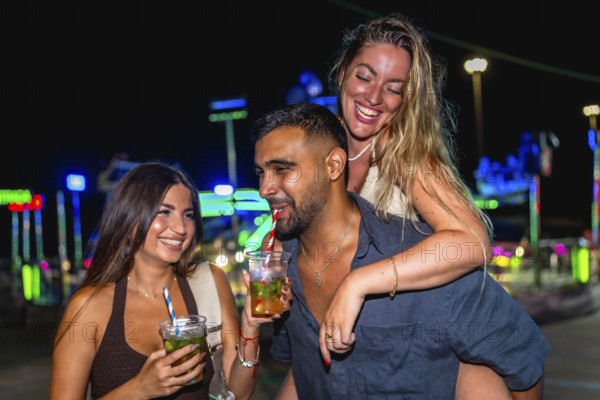 Group of cheerful friends enjoying cocktails and laughing together at an amusement park during a