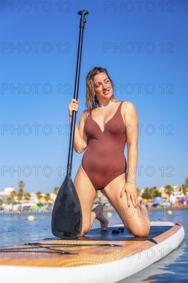 Young woman kneeling on a paddle board, holding a paddle and enjoying a summer vacation at the