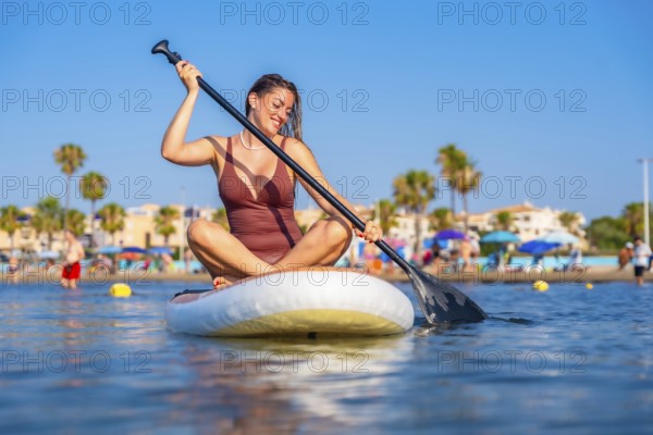 Smiling woman paddling on a stand up paddle board on a sunny summer day at the beach, enjoying her