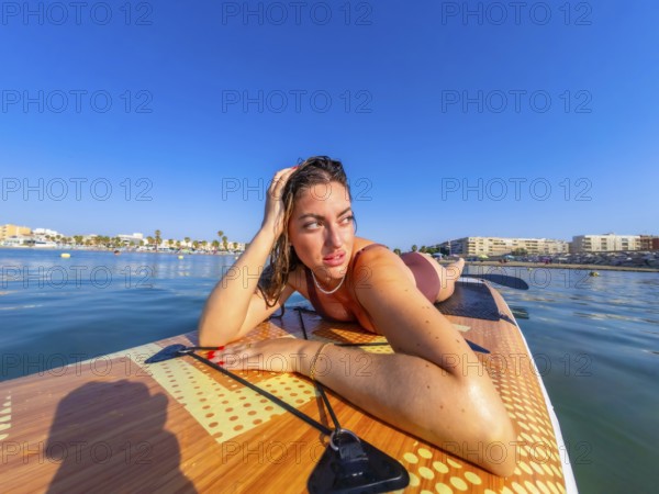 Young woman lying on a paddle board, soaking up the sun and enjoying the serene beauty of the calm