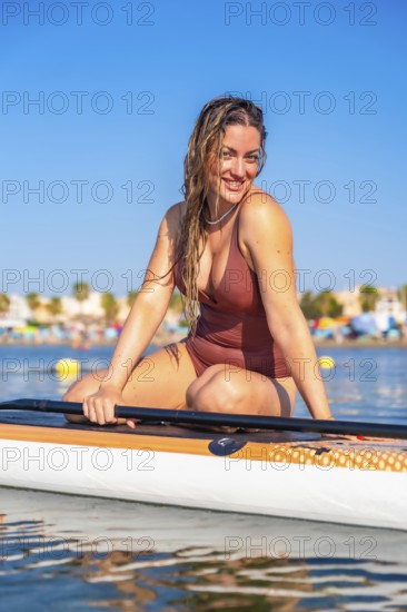 Woman enjoying paddle surfing on a calm sea, smiling under the bright summer sun, with a vibrant